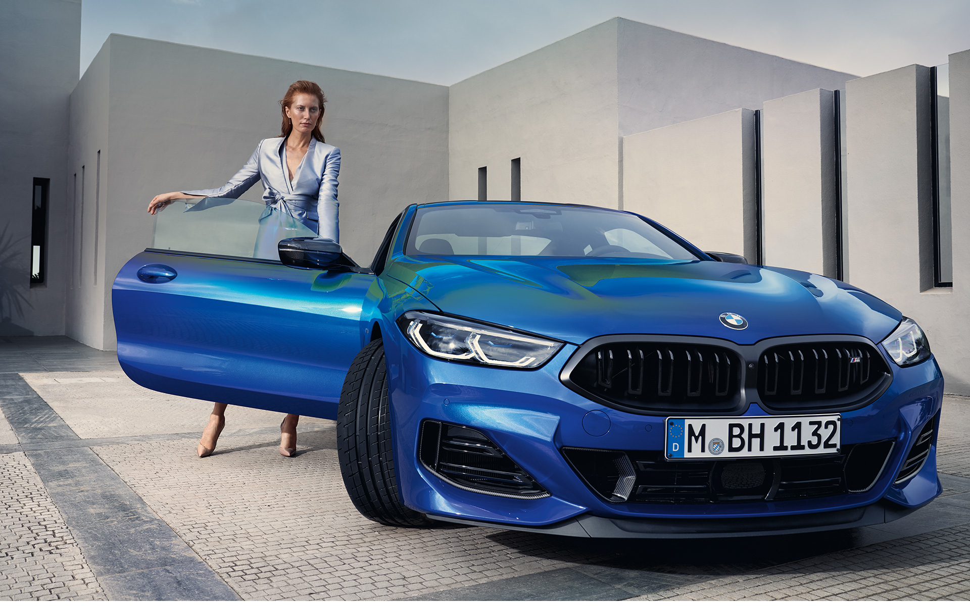 BMW M850i xDrive Coupé G15 LCI Facelift 2022 M Portimao Blue metallizzato vista anteriore da ferma con modella a portiera lato passeggero aperta