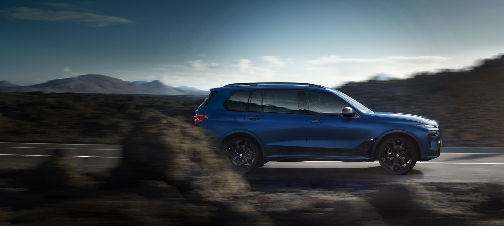 Vista laterale in movimento su strada della BMW X7 M60i G07 LCI in Frozen Marina Bay Blue