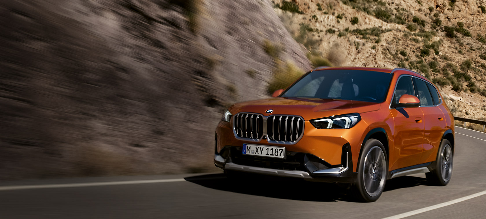 BMW X1 U11 xLine Utah orange metallic Dreiviertel-Frontansicht fahrend auf Landstrasse